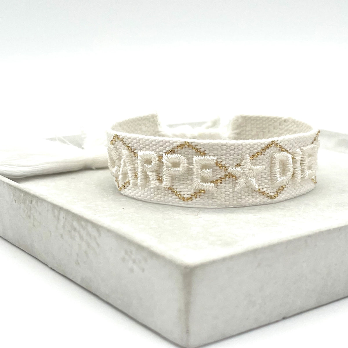 Gewebtes Statement-Armband „CARPE DIEM" in Offwhite mit goldener Stickerei und weisser Quaste – Produktfoto - el encanto