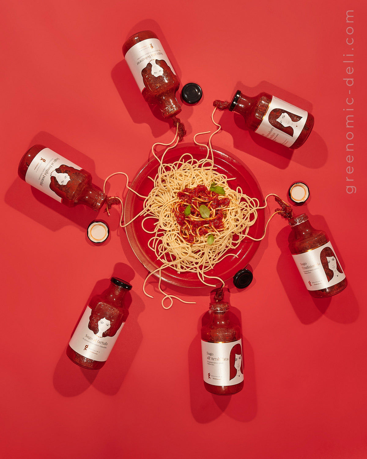 Greenomic Sugo Sortiment – Kreatives Draufsicht-Flatlay 6 Flaschen Sternförmig um Spaghetti-Teller auf Rotem Hintergrund – el encanto